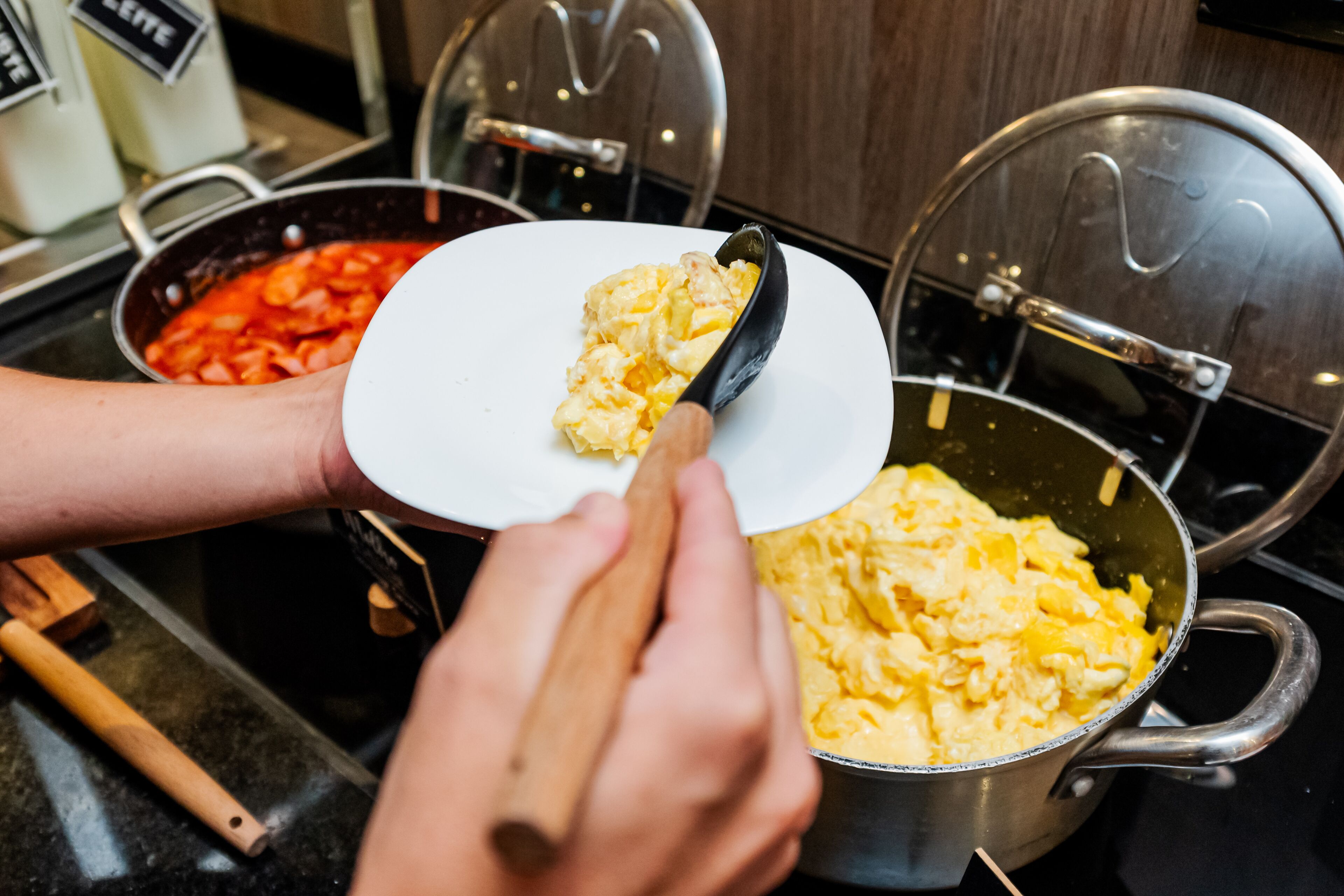 A person scooping scrambled eggs from a pot onto a white plate.