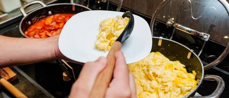 A person scooping scrambled eggs from a pot onto a white plate.