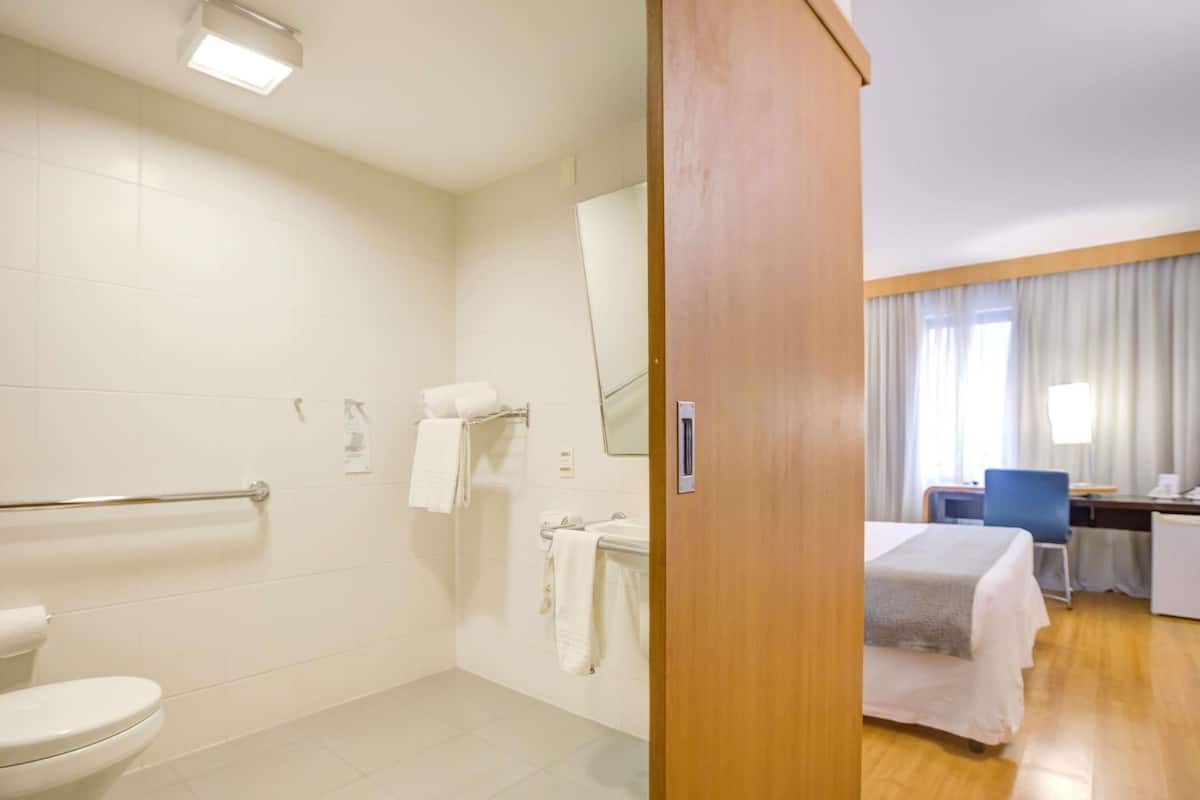 Una habitación de hotel con baño, una cama, un escritorio y una silla.
