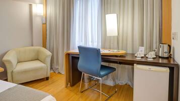 A hotel room with a bed, a desk with a chair, a coffee maker, and a refrigerator.