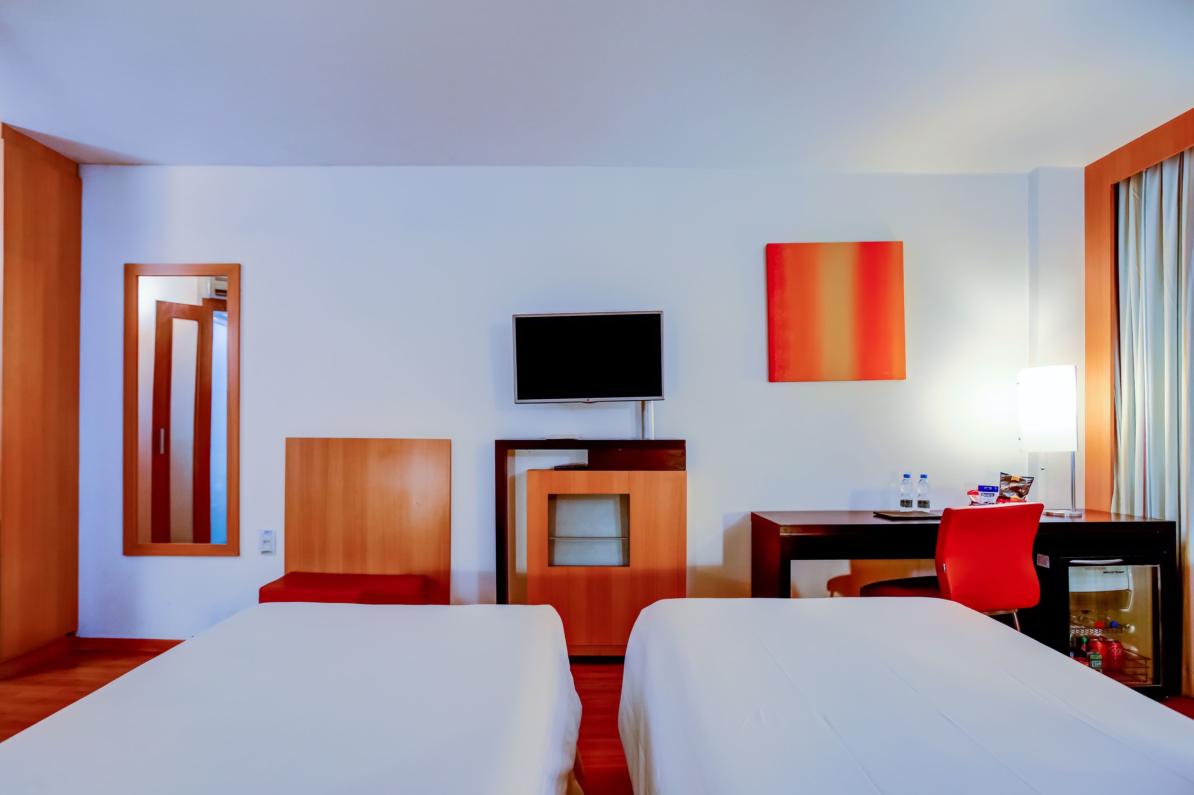 A hotel room with two beds, a desk with a chair, a television, and a minibar.