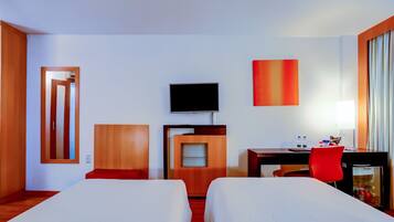 A hotel room with two beds, a desk with a chair, a television, and a minibar.