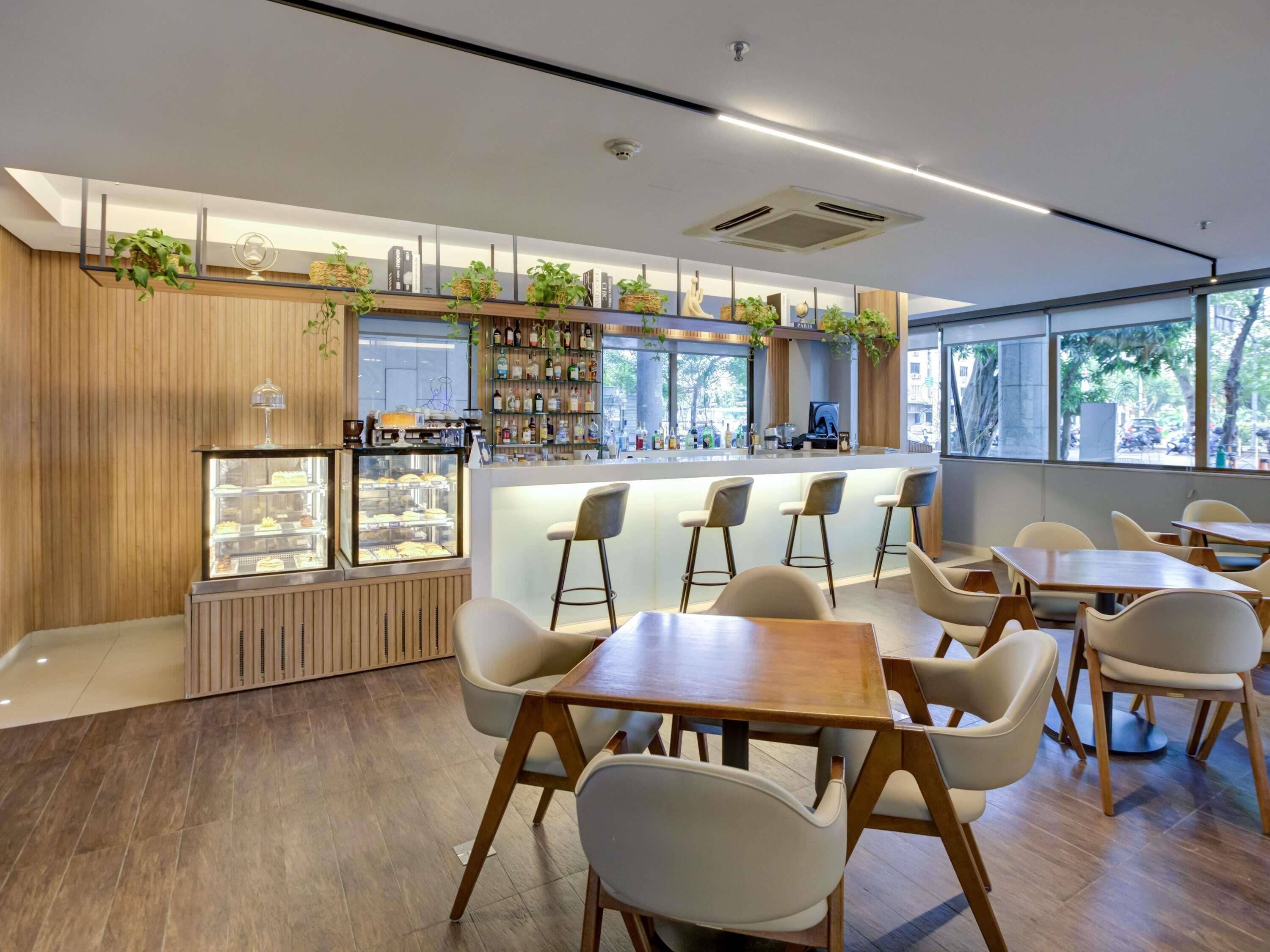Una cafetería moderna con suelo de madera, una barra central con vitrina y varias áreas de estar con mesas y sillas.