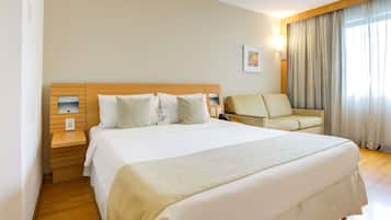 A hotel room with a large bed, a bedside table, a chair, and a window with curtains.