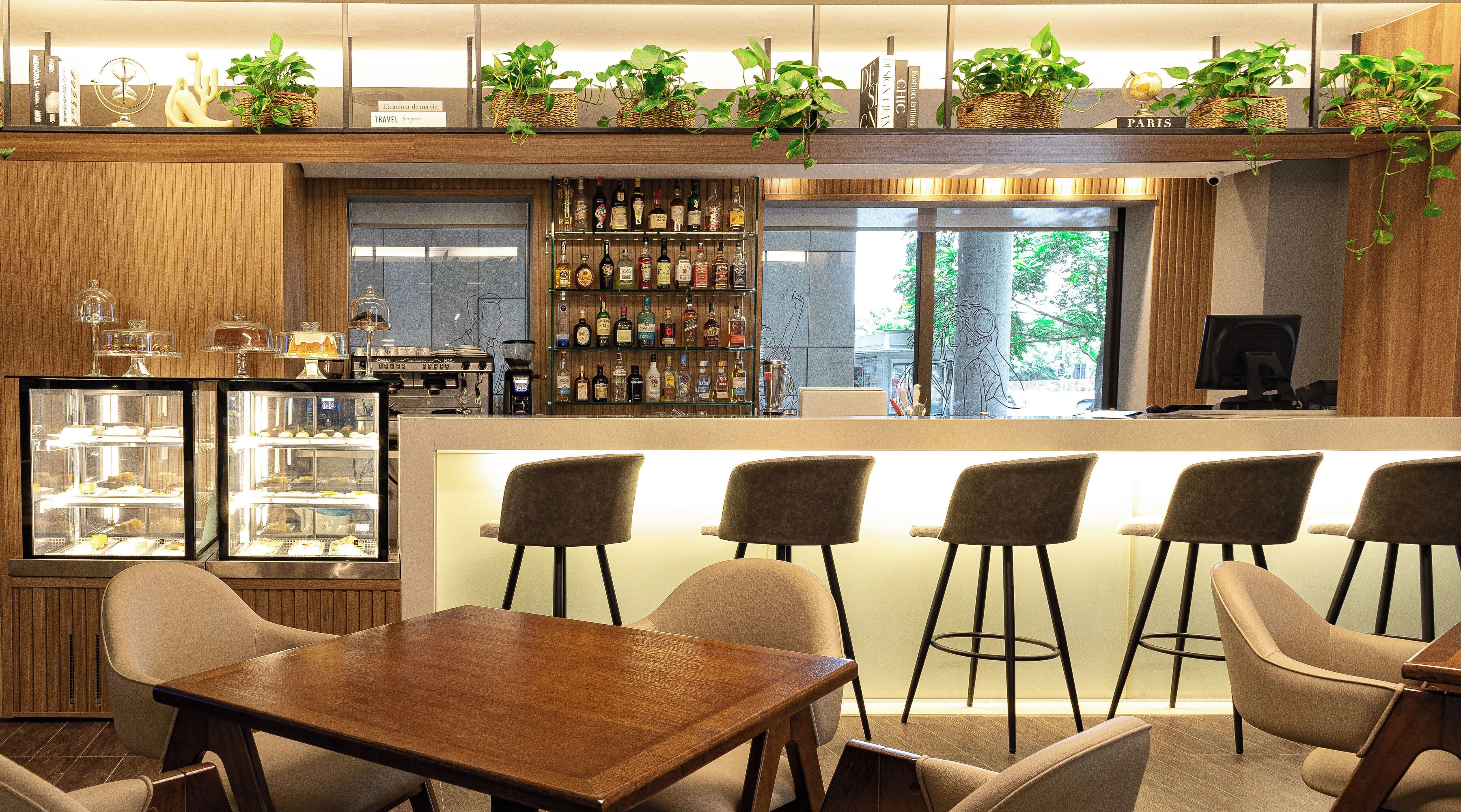 Un área de bar moderna con mostrador de madera, taburetes y una vitrina con pasteles.