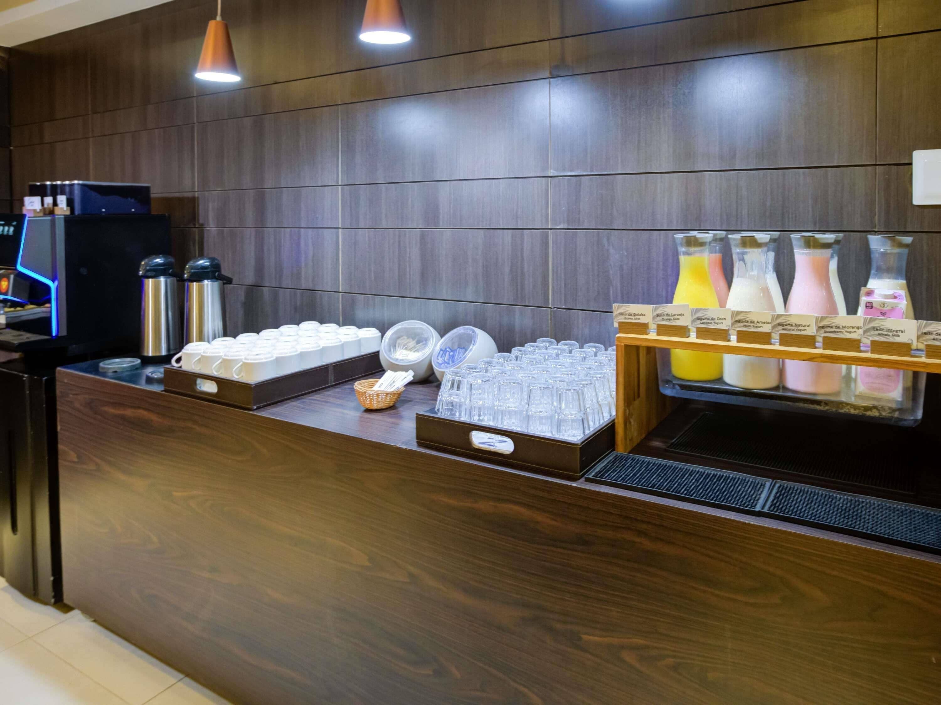 Una estación de café con una máquina de café, tazas térmicas y un dispensador de jugo.