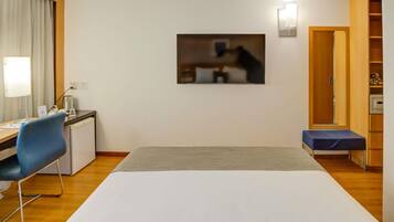 Habitación de hotel con cama, escritorio, silla, mesita de noche, lámpara y un cuadro en la pared.