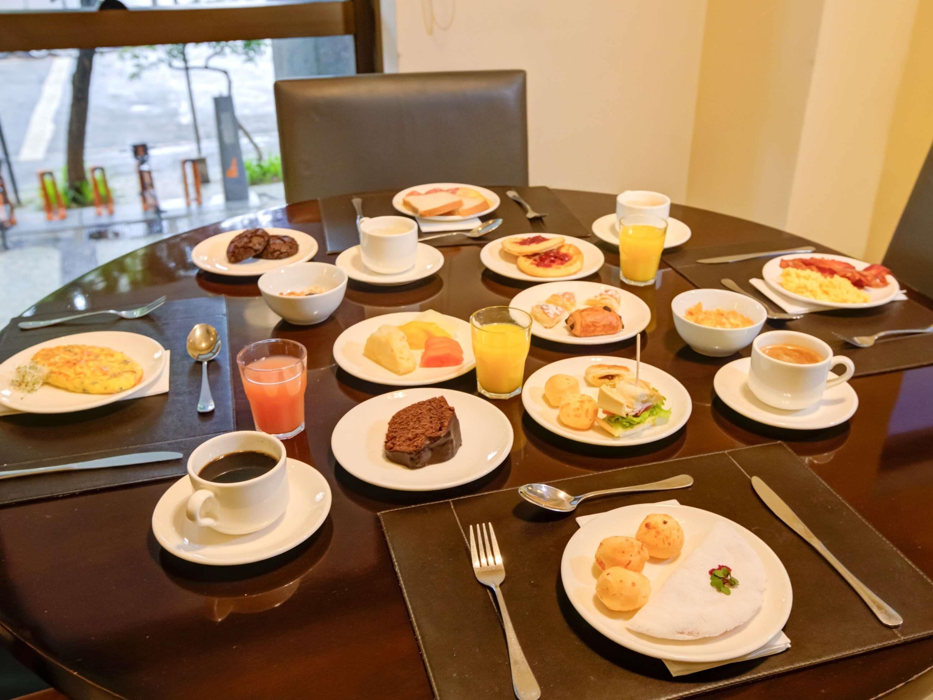 Una mesa redonda para comer con diversas opciones de desayuno, como bollería, frutas y bebidas.