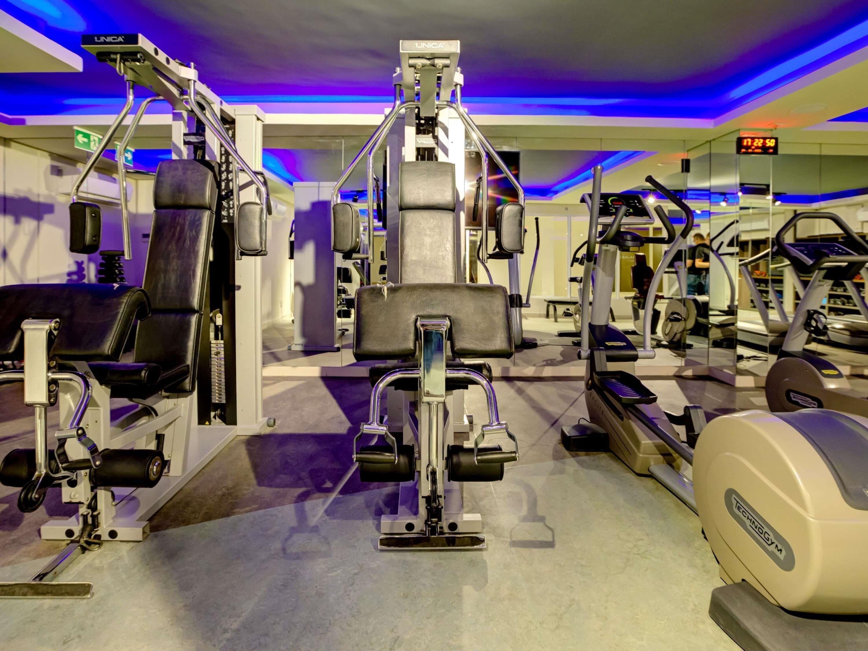 Un gimnasio con diversas máquinas de ejercicio, incluyendo una prensa de banca, una prensa de piernas y una elíptica.