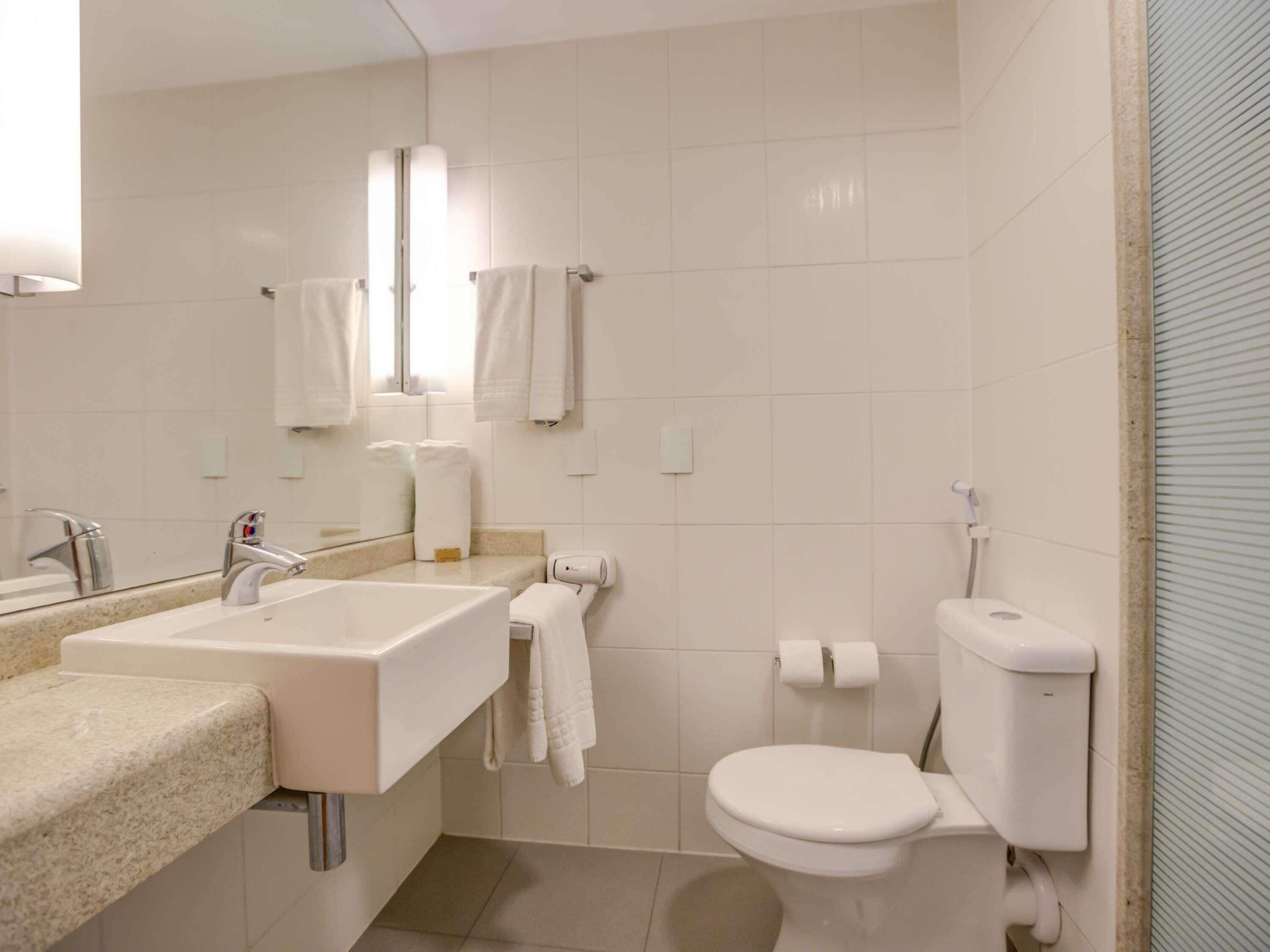 A bathroom with a sink, mirror, towel rack, toilet, and a towel dispenser.