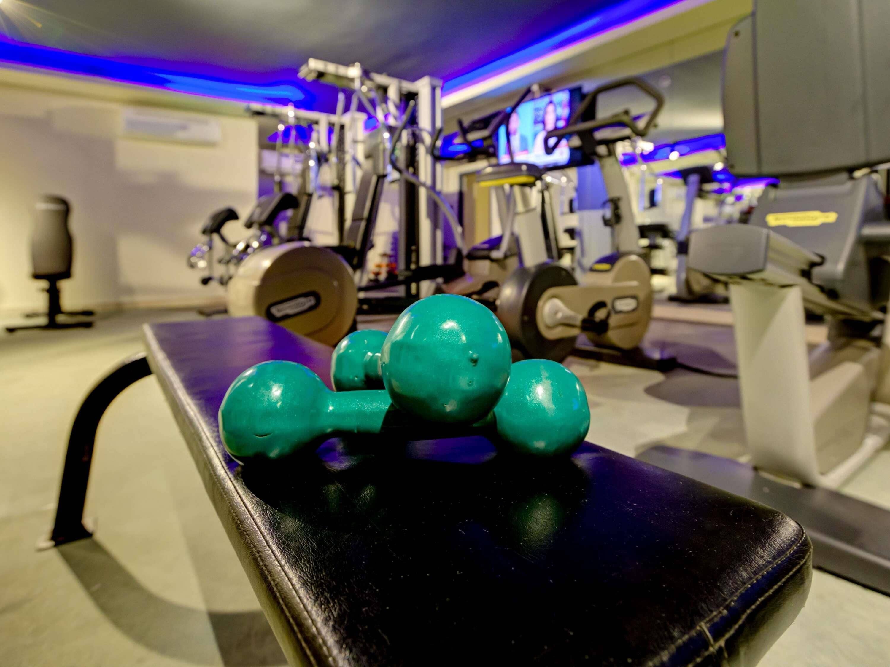 Un gimnasio con equipo de ejercicio y mancuernas sobre un banco.