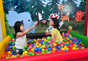 Two children playing in a colorful ball pit with a jungle-themed mural in the background.