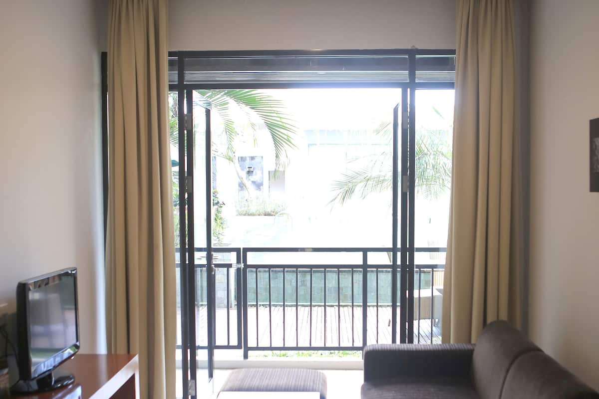 Ein Wohnzimmer mit einer Couch, einem Fernseher auf einem Schreibtisch und einem Balkon mit Blick ins Freie.