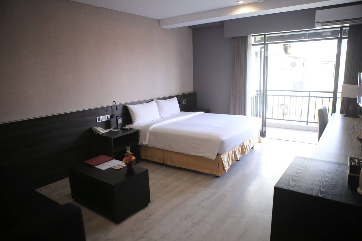Ein Hotelzimmer mit Bett, Nachttisch, Lampe und Blick ins Freie.