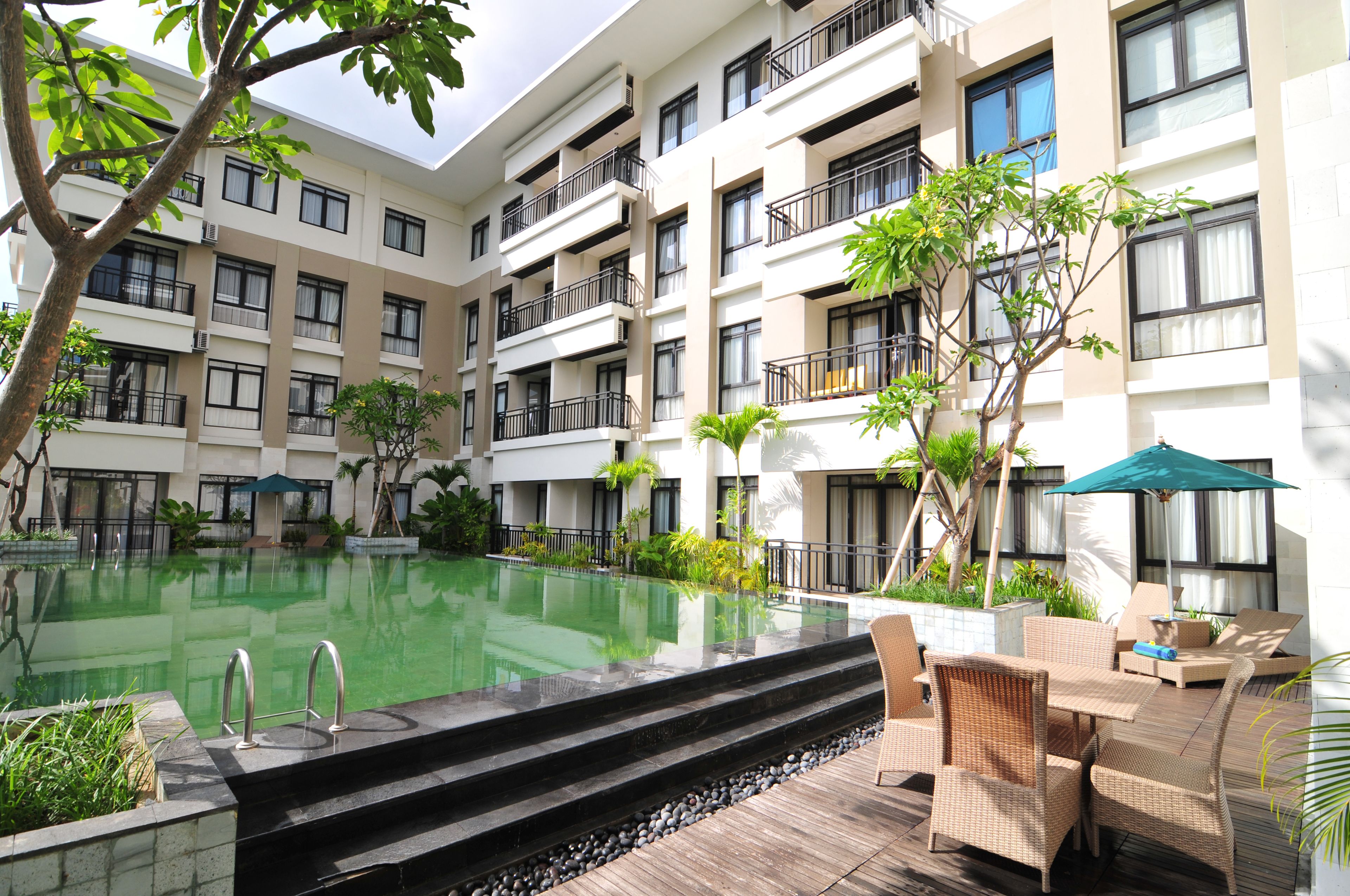 A multi-story hotel with a central swimming pool, outdoor seating area, and balconies.