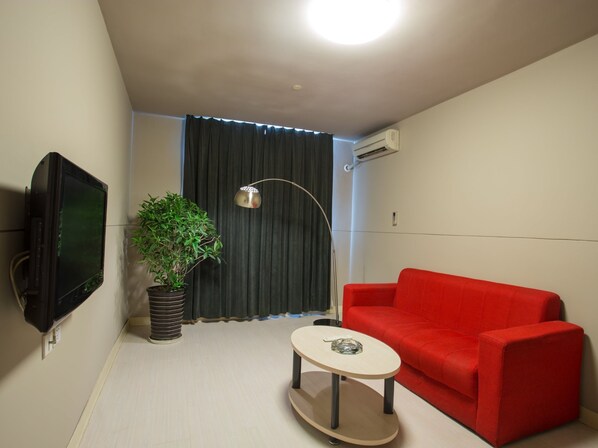 A small, modern living room with a red sofa, a small round table, a potted plant, a TV mounted on the wall, and a ceiling light. - Jinjiang Inn Tianjin Hongqiao Guangrongdao (Tianjin)