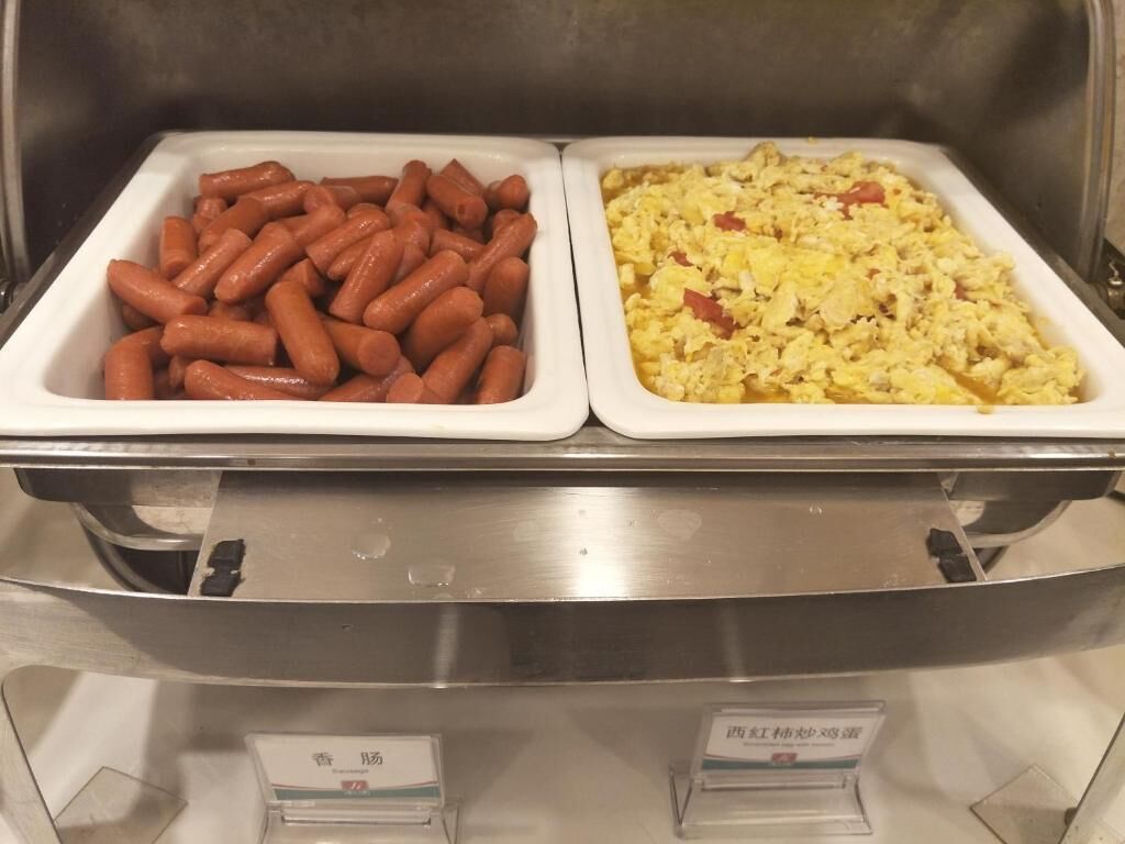 Two food dispensers with hot dogs and scrambled eggs.