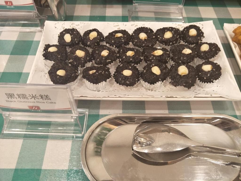 Bandeja de pasteles de arroz glutinoso negro con cubiertas blancas, etiquetados como 'Black Glutinous Rice Cake'.
