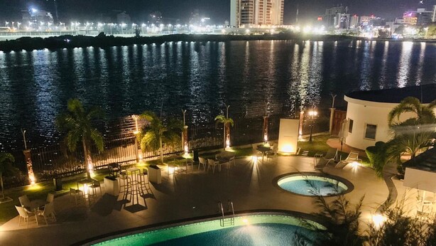 A nighttime view of a hotel pool area with a large pool and a smaller circular pool, surrounded by lounge chairs and palm trees. - Hotel Bon Voyage (Lagos)