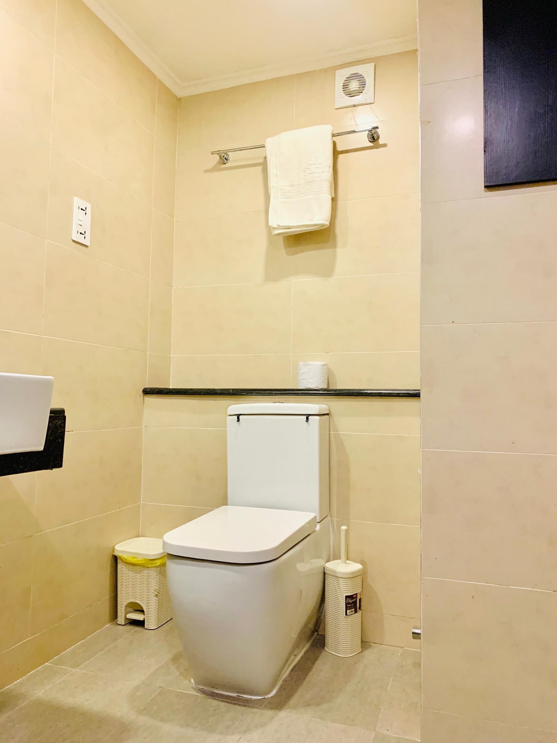 Une petite salle de bain propre, équipée de toilettes, d’une petite poubelle, d’un distributeur de mouchoirs et d’un porte-serviettes.