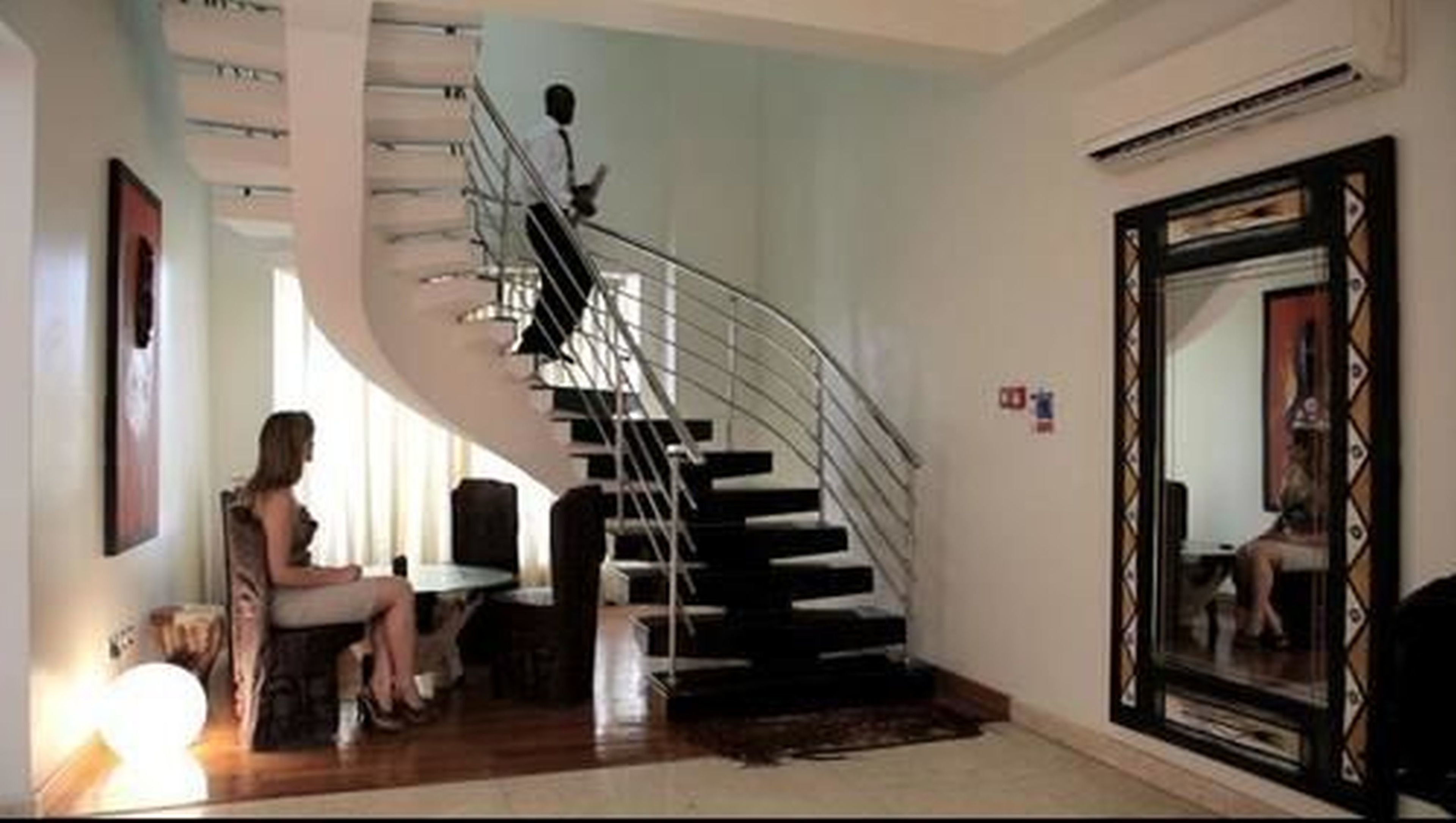 A modern interior with a curved staircase, a dining area, and a large mirror.