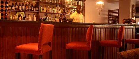 A bar area with wooden paneling, red upholstered chairs, and a bartender preparing drinks.