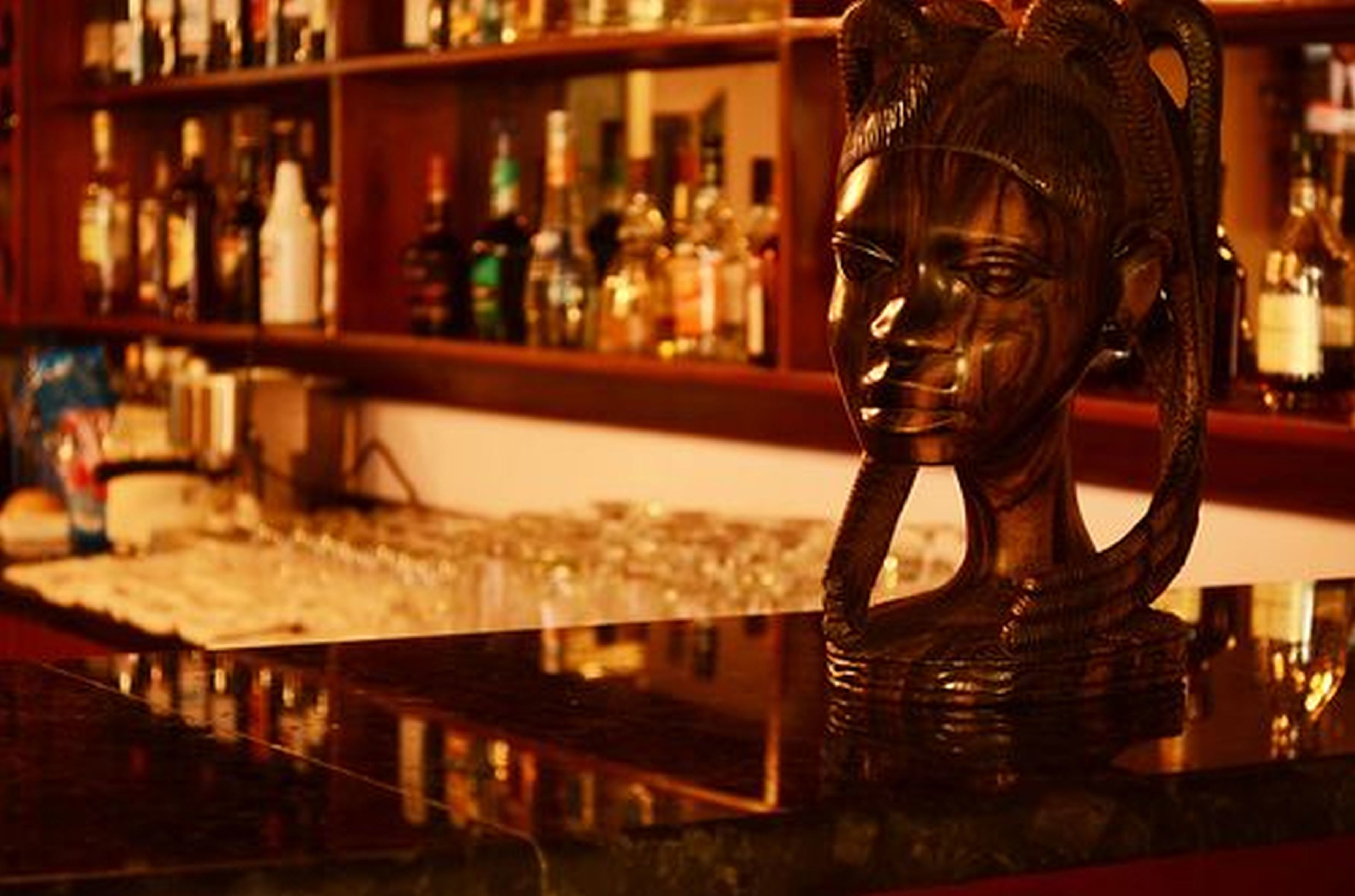 A bar with a wooden head sculpture and shelves of liquor bottles.