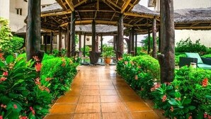 A covered walkway with a tiled floor, surrounded by lush greenery and potted plants. - Hotel Bon Voyage (Lagos)