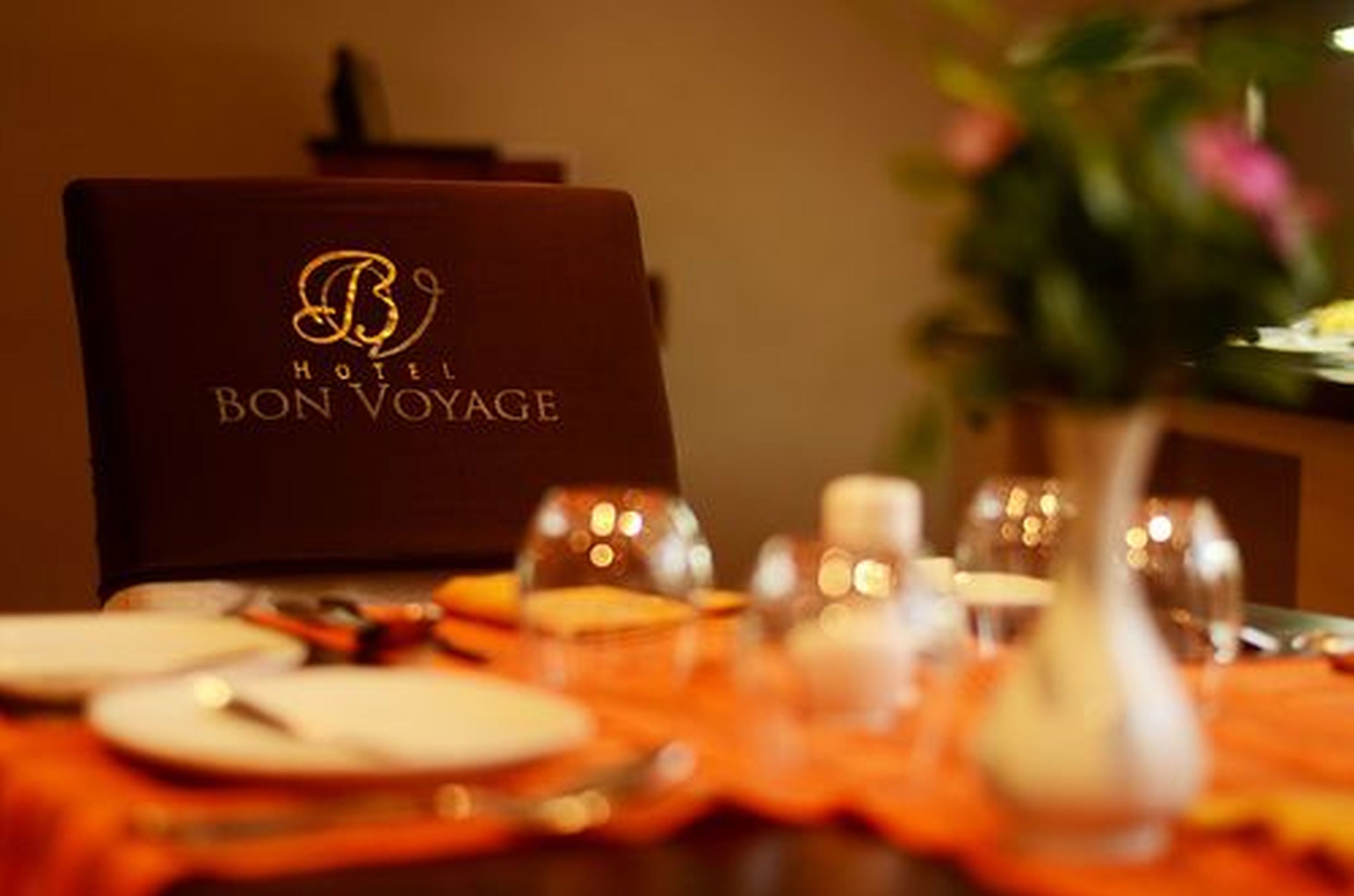 A hotel room with a table set for dining, featuring a logo on the wall and a vase with flowers.