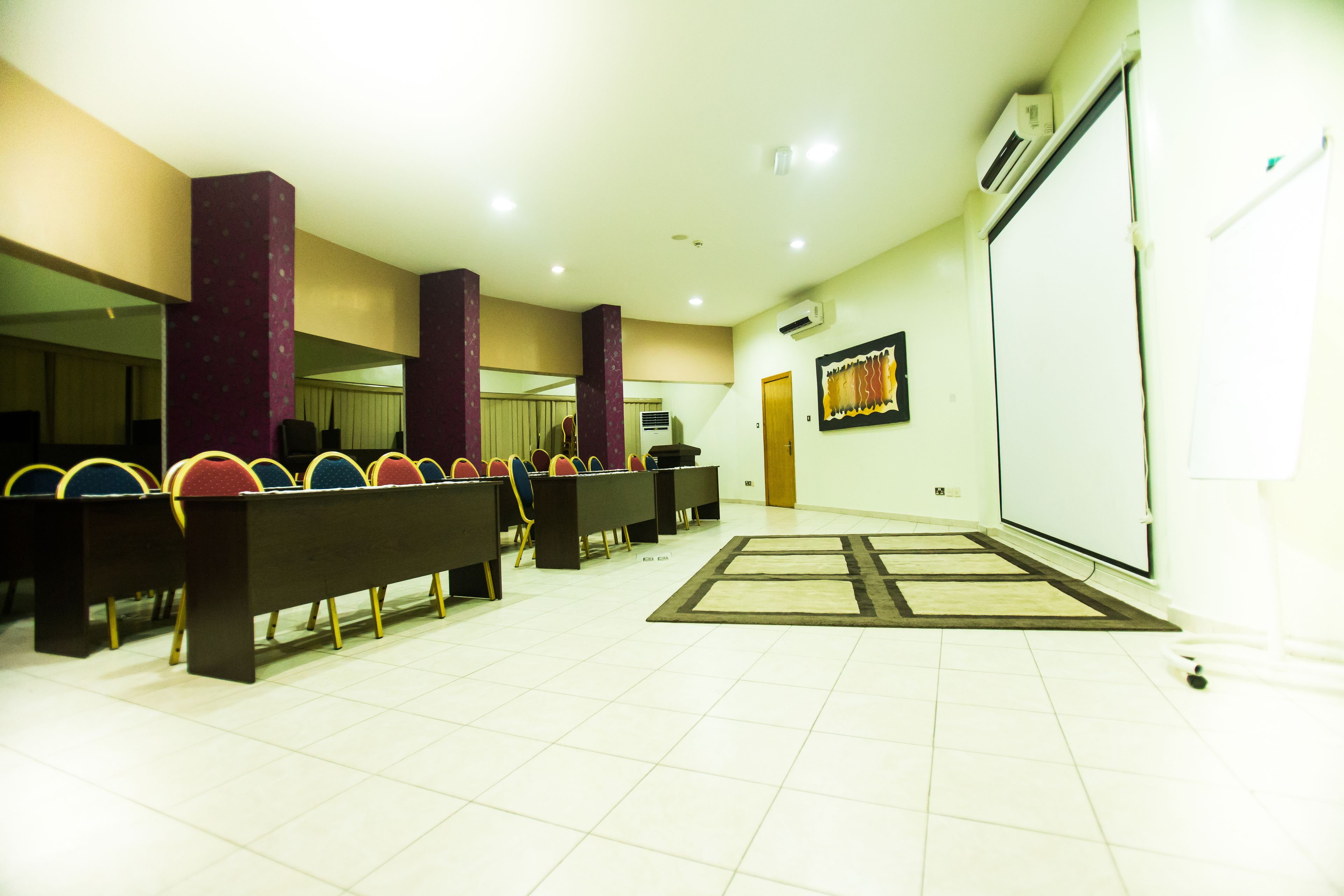 A conference room with rows of chairs, a projector screen, and a whiteboard.