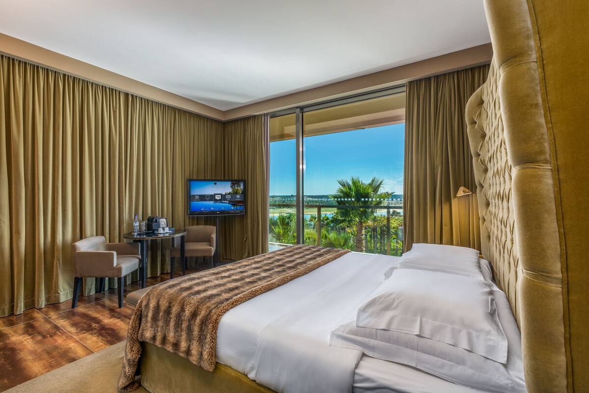 A hotel room with a large bed, a desk with a television, and a view of the outdoors.