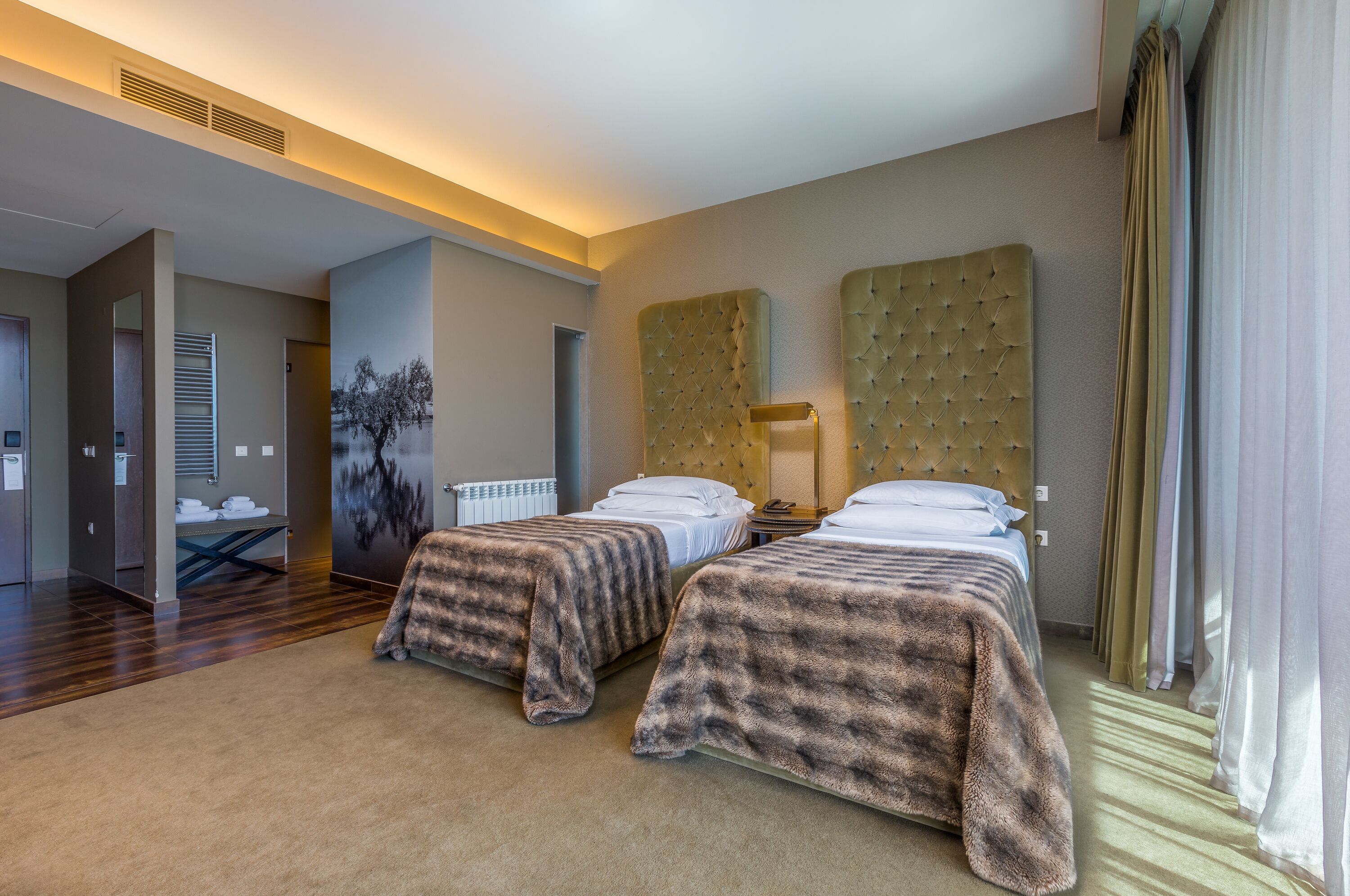 A hotel room with two beds, a large headboard, a painting on the wall, and a view of the hallway.