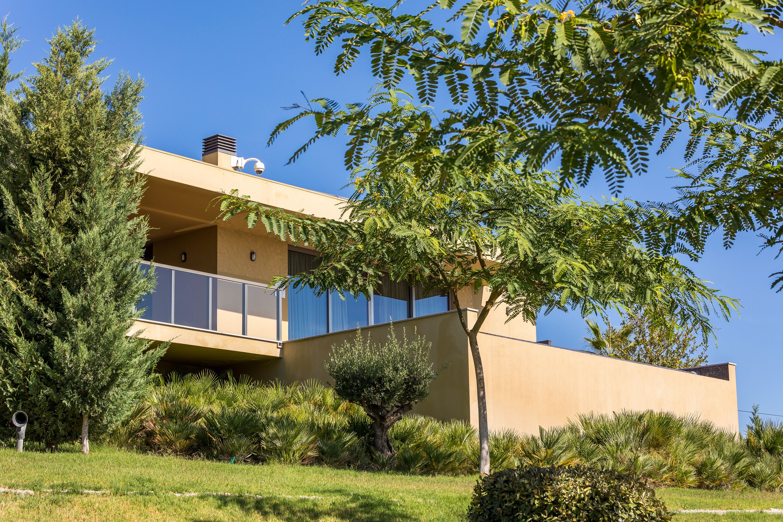 A modern building with a flat roof, large windows, and a well-maintained garden with various plants and trees.