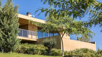 A modern building with a flat roof, large windows, and a well-maintained garden with various plants and trees.