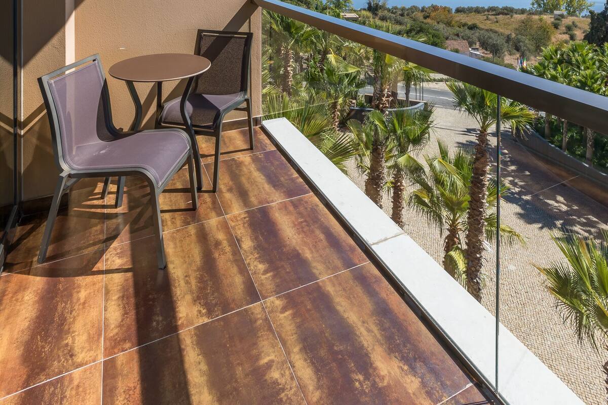 A balcony with a table and chairs, overlooking a beach and palm trees.