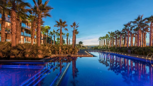 A pool with palm trees and a building in the background. - AP Lago Montargil Conference & Spa (Ponte de Sor)