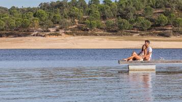 A couple sitting on a concrete platform in a calm body of water, with a forested hillside in the background.