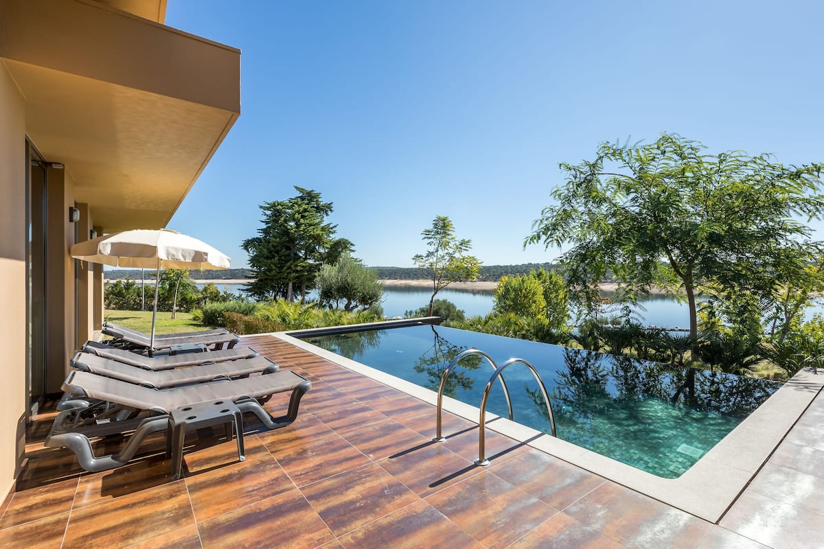 A modern outdoor pool area with lounge chairs and a view of a lake.
