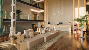 A modern hotel lobby with a large sectional sofa, a reception desk, and a wooden wall with the hotel name.