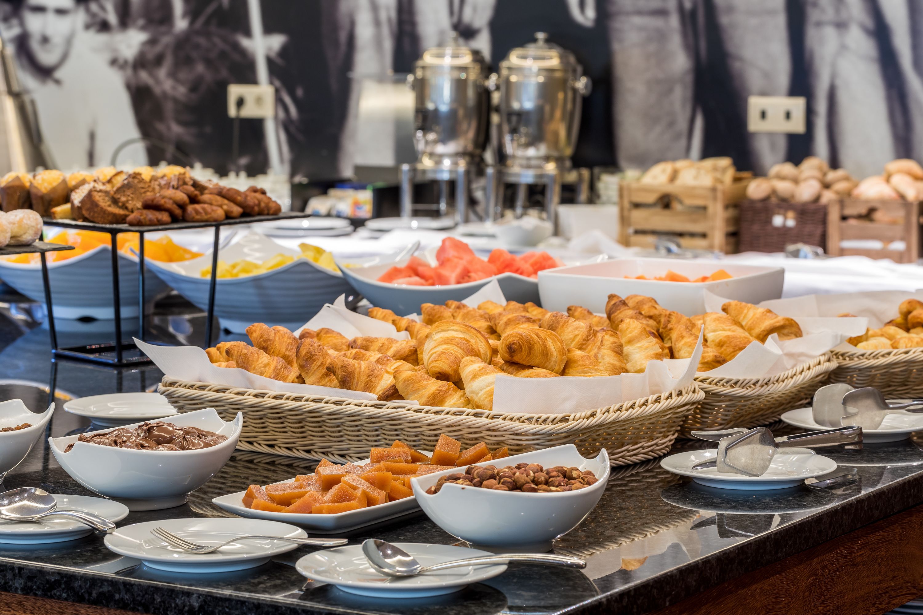 A buffet with various food items including croissants, fruits, and pastries.