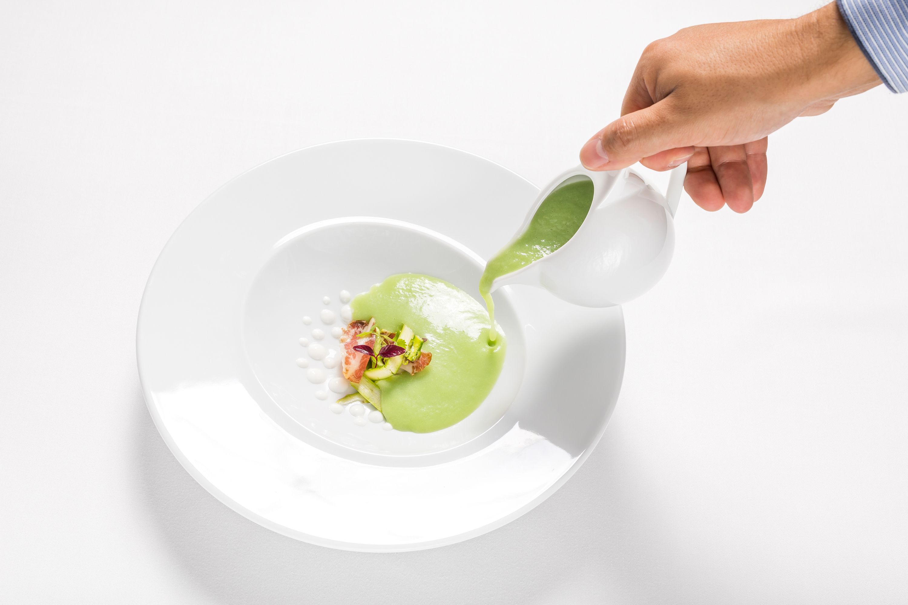 A hand pouring a green sauce onto a white plate with a dessert.