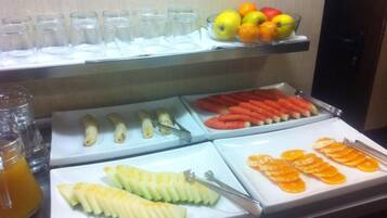 A buffet with various fruits and vegetables, including sliced apples, oranges, and carrots.