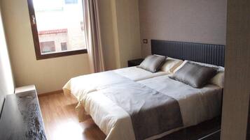 Een slaapkamer met een bed, nachtkastje en raam met gordijnen.