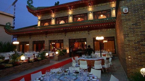 An outdoor dining area with tables set for a meal, a brick building with traditional architectural elements, and a red carpet leading to the entrance. - Hotel Dinastía (Getafe)