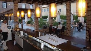 An outdoor dining area with brick walls, hanging lights, and tables with chairs. - Hotel Dinastía (Getafe)