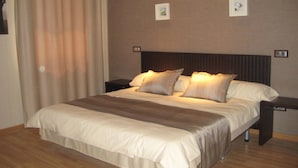 A neatly made bed with a striped bedspread and two pillows, a wooden floor, and a wall with two framed pictures. - Hotel Dinastía (Getafe)