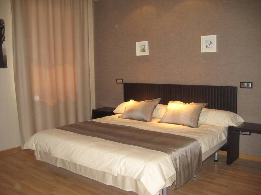 Uma cama bem arrumada com um edredom listrado e dois travesseiros, piso de madeira e uma parede com duas molduras.