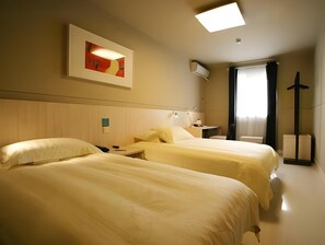 Habitación de hotel con dos camas, una mesita de noche, una lámpara, un cuadro en la pared y una ventana con cortinas.