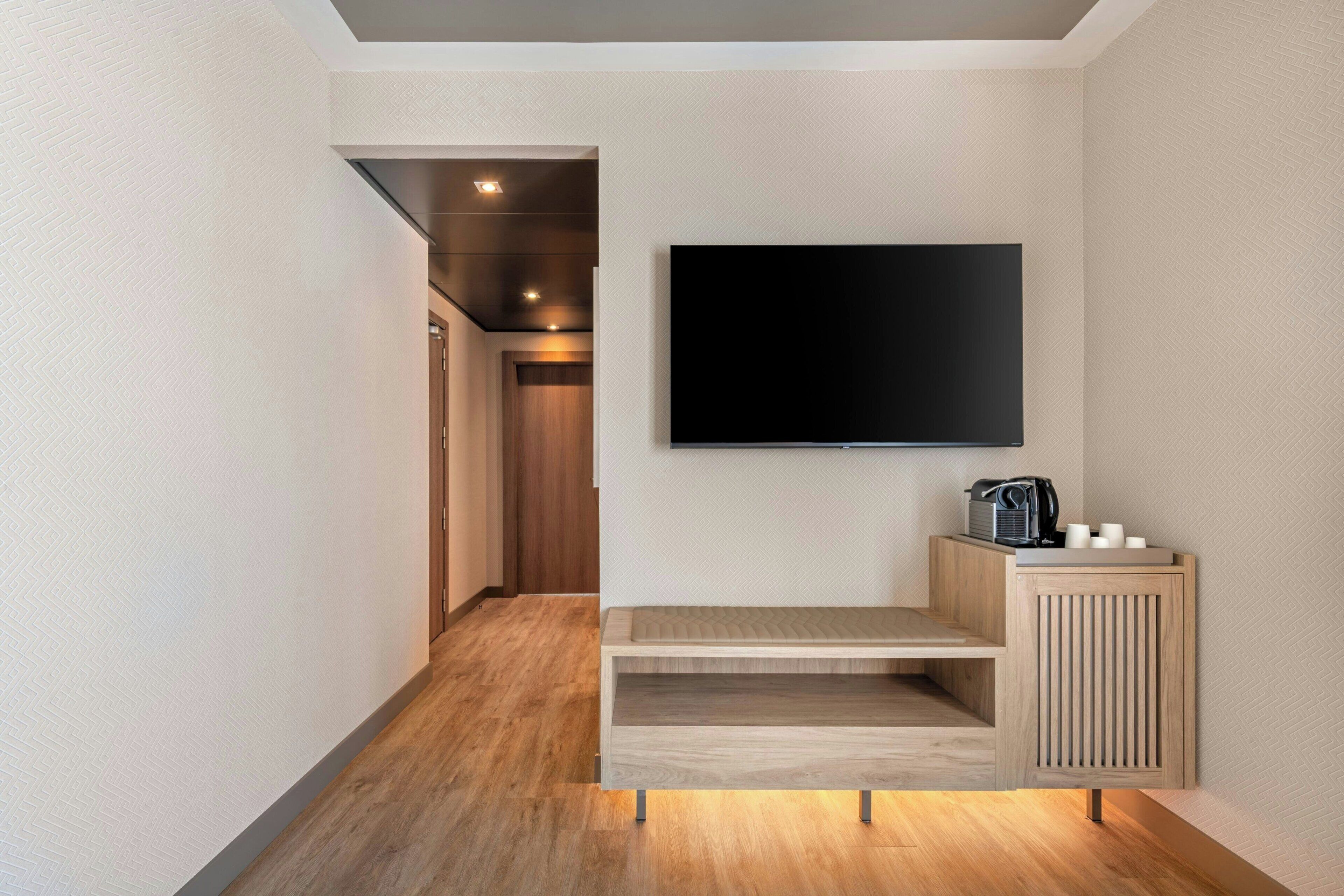 Et moderne hotelværelse med et fladskærms-TV monteret på væggen, et trækonsolbord og en gang der fører til en dør.