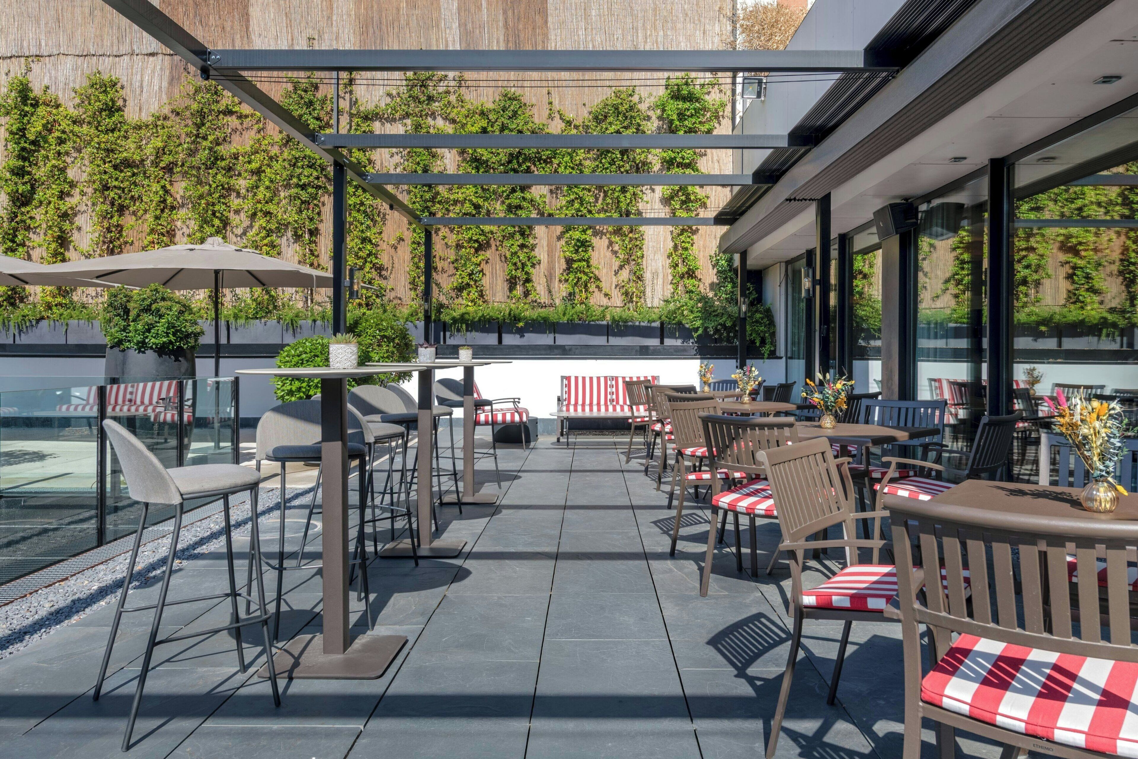 Une terrasse extérieure avec des tables et des chaises, une pergola et une vue sur un bâtiment à la façade en bois.